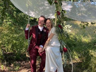 Alexander Vlahos and Julia Huard are sitting in a swing in their wedding dress.